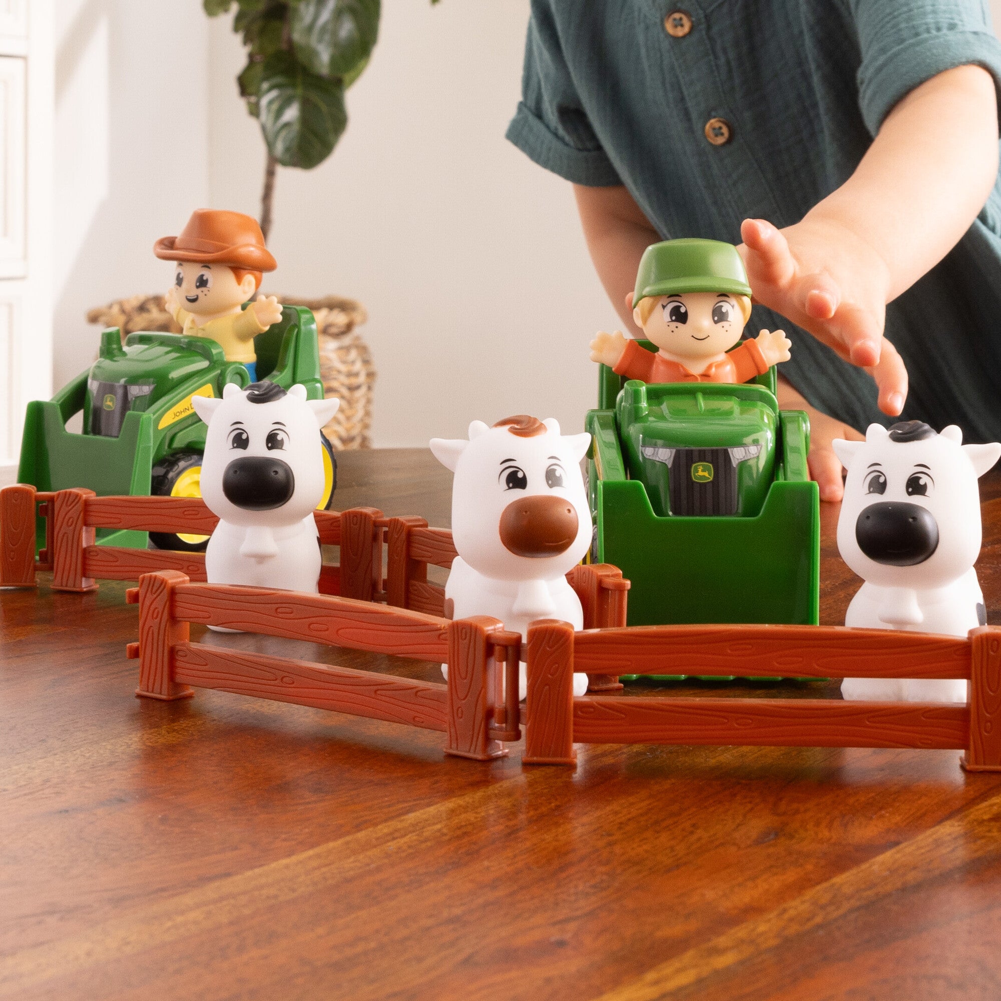 Child's hand reaching for the John Deere Cows Are Out Playset Farmer