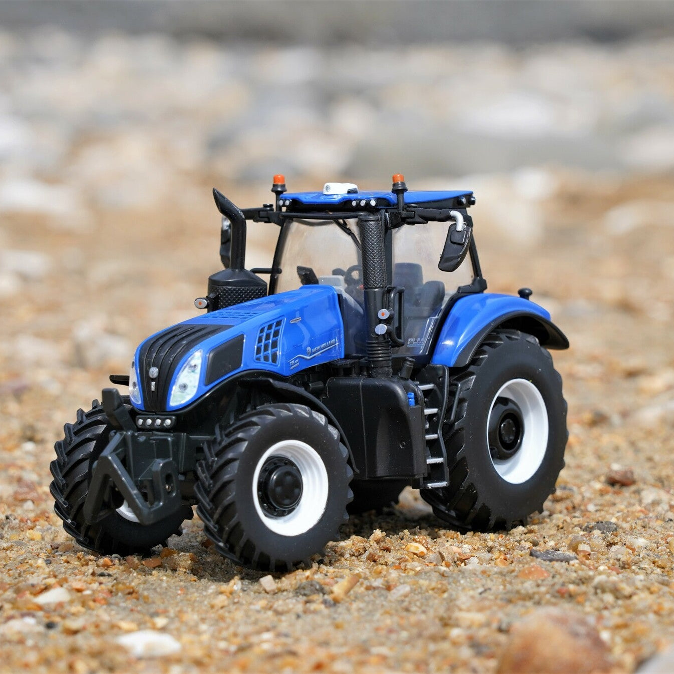 Blue Britains New Holland toy tractor on a sandy surface